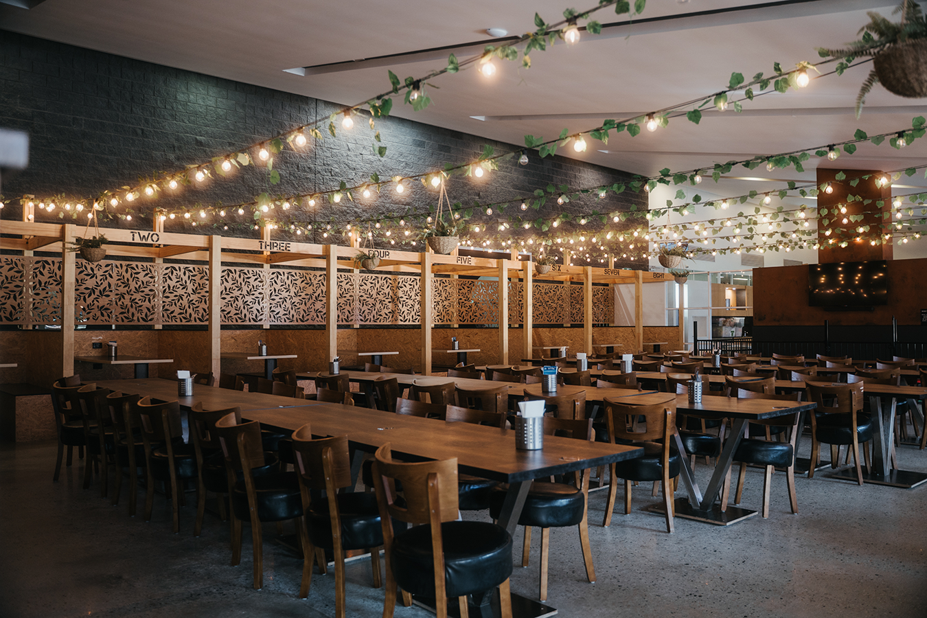 Indoor dining area at ROAR Bar & Grill featuring long wooden tables, booth seating, and warm string lights with hanging greenery creating a cosy, welcoming atmosphere.