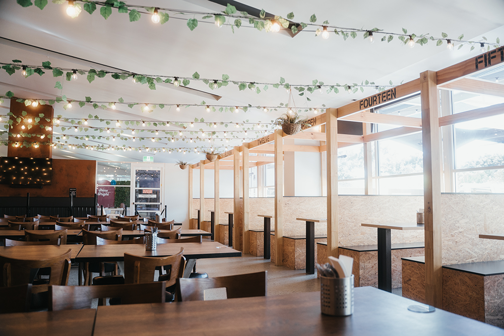 Indoor dining area at ROAR Bar & Grill featuring wooden tables and chairs, numbered booth-style seating, and hanging string lights with green leaf decorations creating a warm and inviting atmosphere.